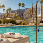 Palm Springs resort pool with an IV drip beside a lounge chair, desert mountains and palm trees in the background